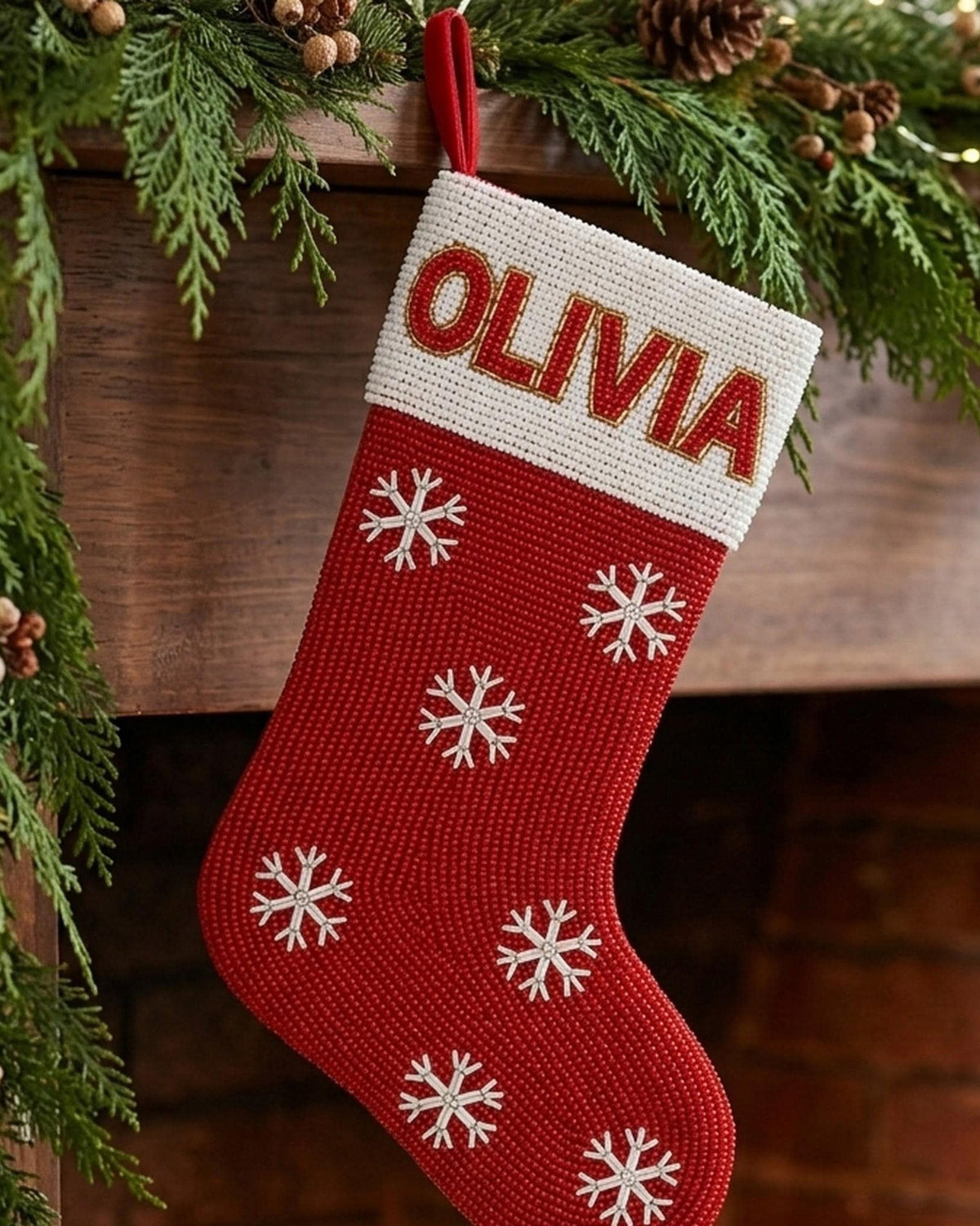 Hand-beaded red velvet Christmas stocking with a name on the cuff hanging from a mantel