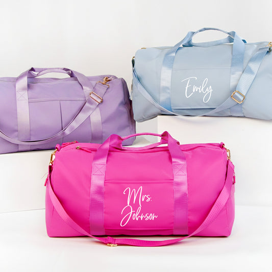 three colorful duffel bags, each with a personalized name printed on it.