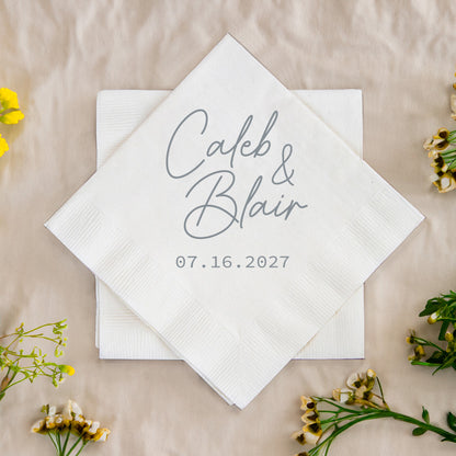 White napkin with 'Caleb & Blair 07.16.2027' text on a beige background with flowers.