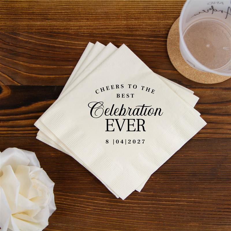 Stack of napkins with 'Cheers to the best celebration ever' text on a wooden table with flowers and a glass.
