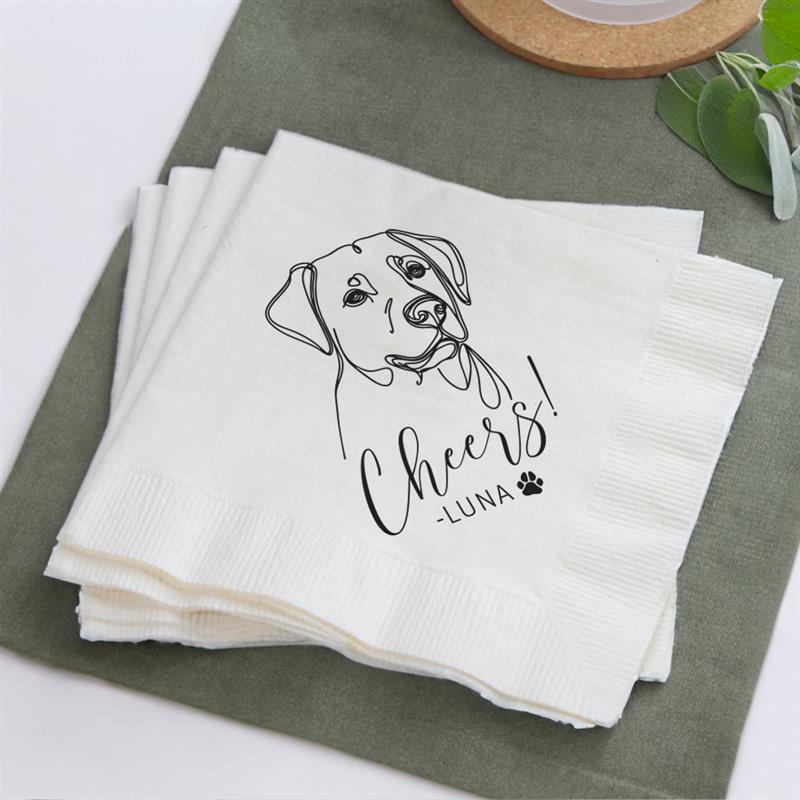 Stack of white napkins with a dog illustration and 'Cheers Luna' text on a green surface.