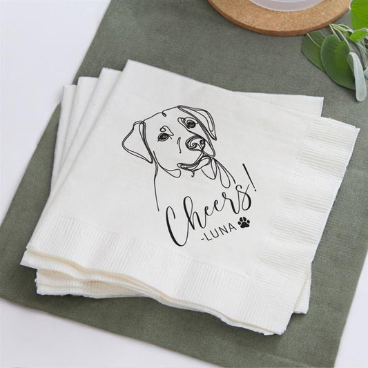 Stack of white napkins with a dog illustration and 'Cheers Luna' text on a green surface.