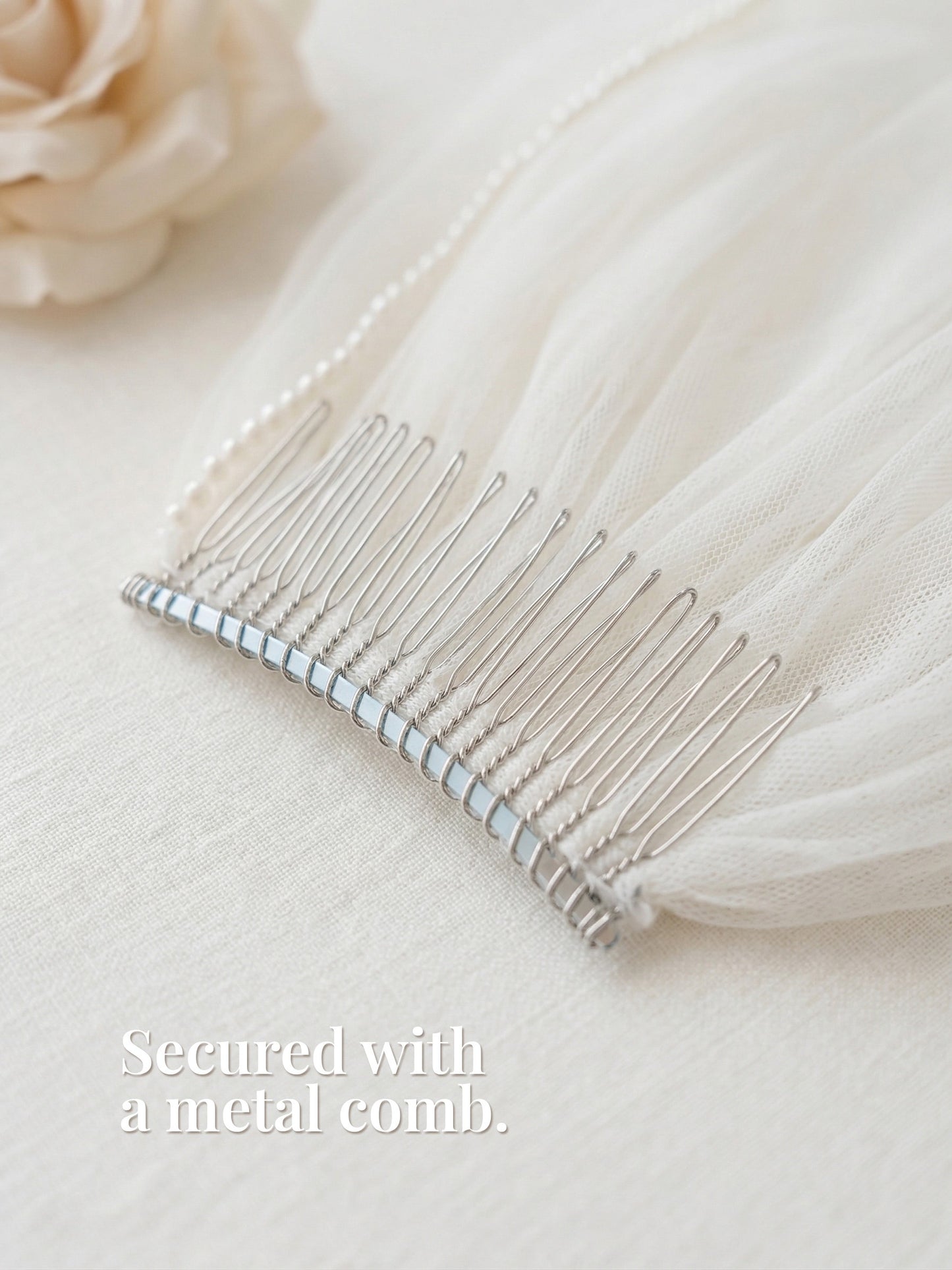 A silver metal comb rests on a white fabric, secured with a pearl bead.