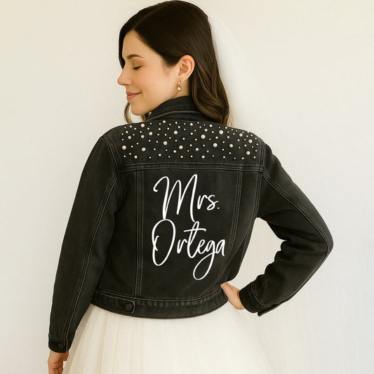 Woman wearing a black denim jacket with 'Mrs. Ortega' on the back against a white background
