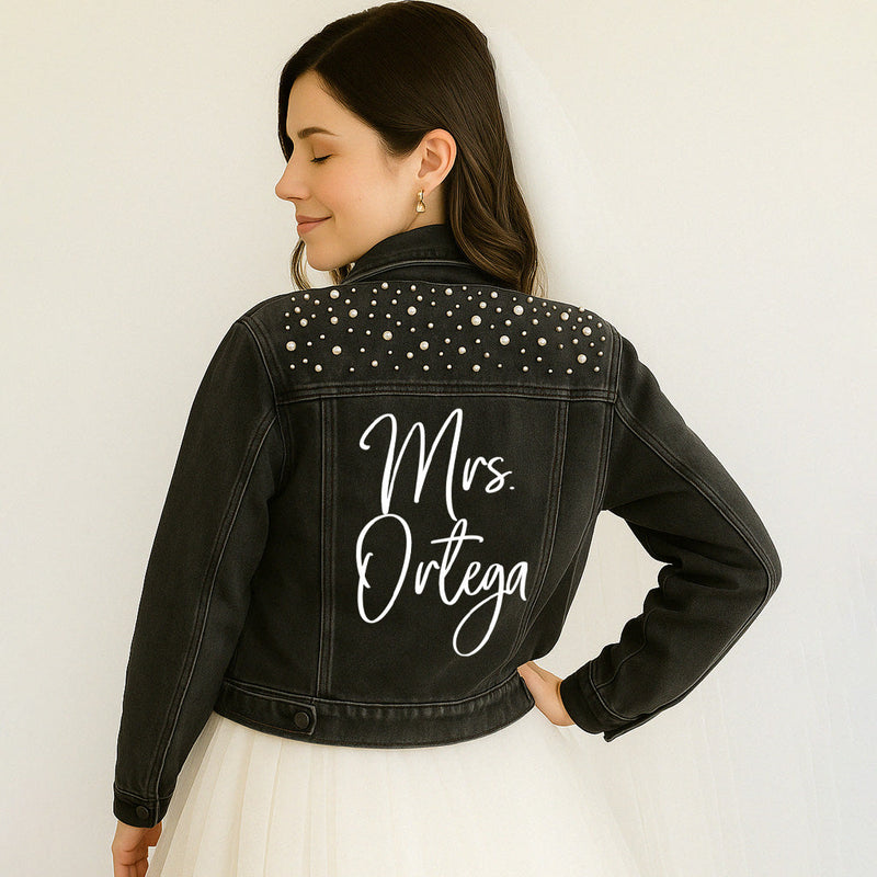 Woman wearing a black denim jacket with 'Mrs. Ortega' on the back against a white background