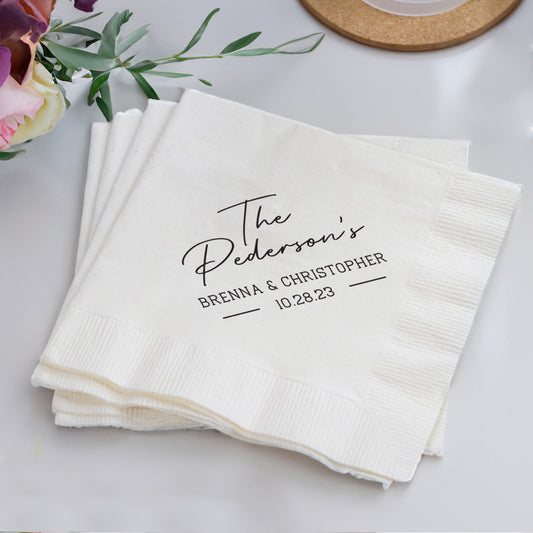 Stack of personalized napkins with names and date on a white surface with flowers.