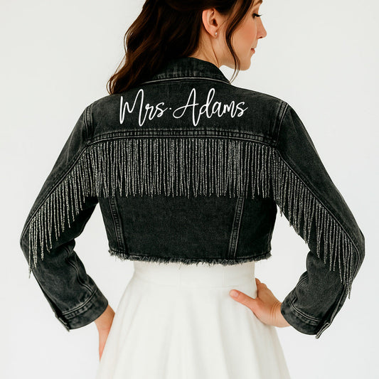 Black denim jacket with fringe details and 'Mrs. Adams' embroidery on a plain background