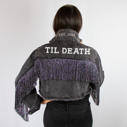 A denim jacket with black fringe and a custom patch reading 'TIL DEATH' on the back, worn by a person facing away from the camera.