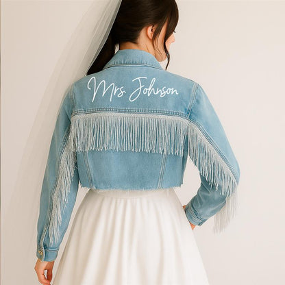 A blue fringe denim jacket with 'Mrs Johnson' printed on the back, worn over a white garment, possibly a dress.