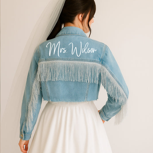 A blue denim jacket with fringe detailing on the back, featuring the text 'Mrs. Wilson' printed on the collar