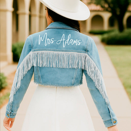 Person wearing a denim jacket with 'Mrs. Adams' embroidered on the back, standing outdoors.