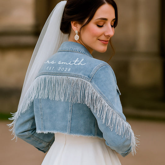 A woman wearing a blue denim jacket with fringe details on the sleeves and back, customized with white text on the back collar.