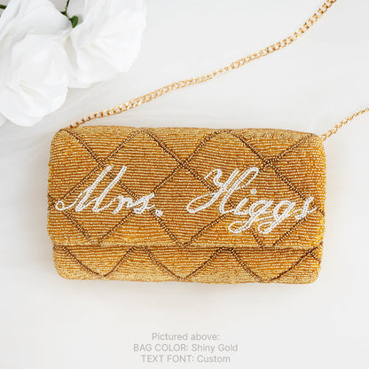 A gold-colored handbag with the names 'Mrs. Higgs' written on it in cursive script.