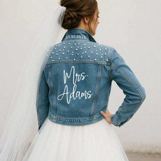 Woman wearing a blue denim jacket with 'Mrs. Adams' and a date on the back, standing against a plain background.