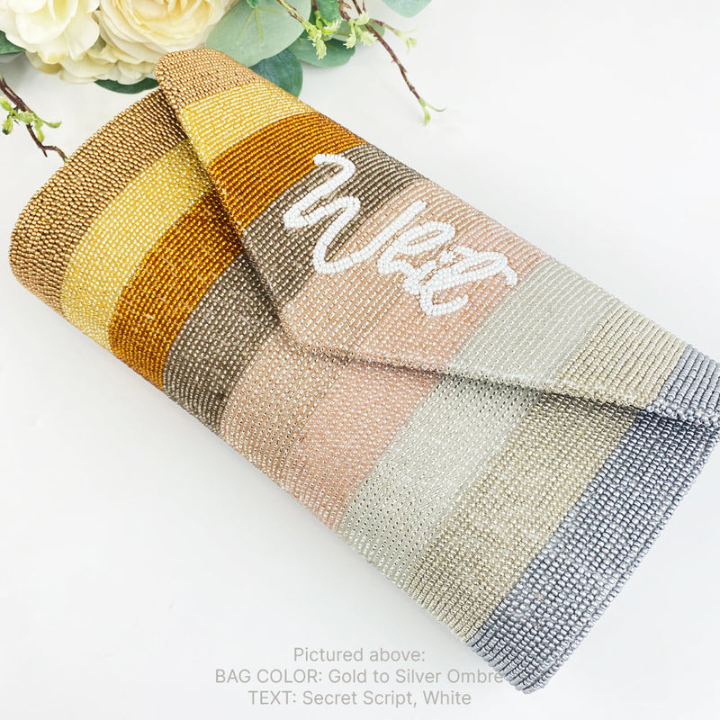 A colorful striped clutch purse with the word "West" written on it, placed on a white surface next to some flowers.