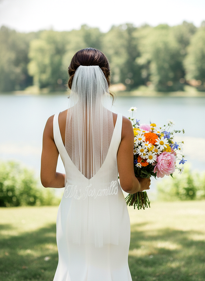 A bride in a white wedding dress holds a bouquet of colorful flowers and stands in front of a serene lake surrounded by lush greenery.