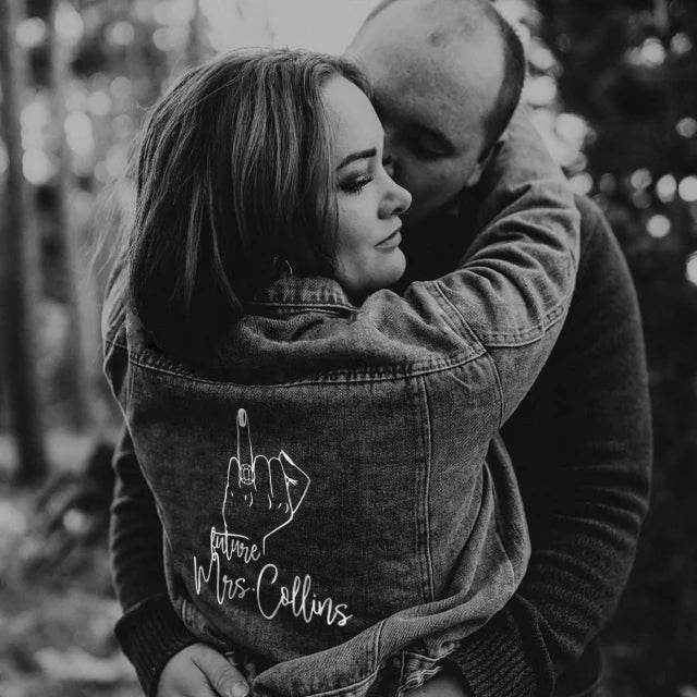 Black and white photo of a couple embracing with a woman wearing a jacket with 'Future Mrs Collins' text.