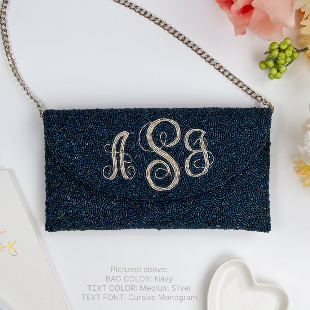 a navy blue clutch purse with a monogrammed initials on it, placed on a white surface alongside some flowers and a heart-shaped object.