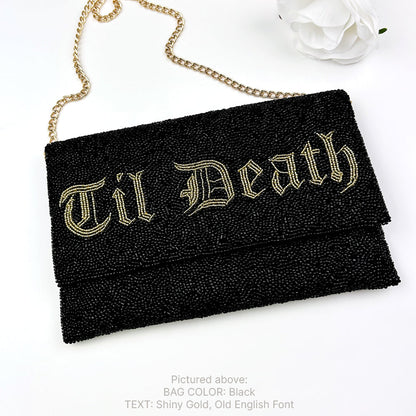 A black clutch purse with the text "Til Death" embroidered on it in an ornate gold font.