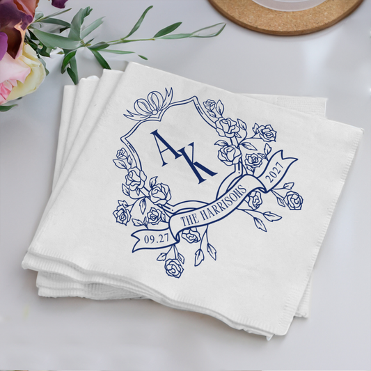Stack of white napkins with blue floral design and monogram on a light surface.