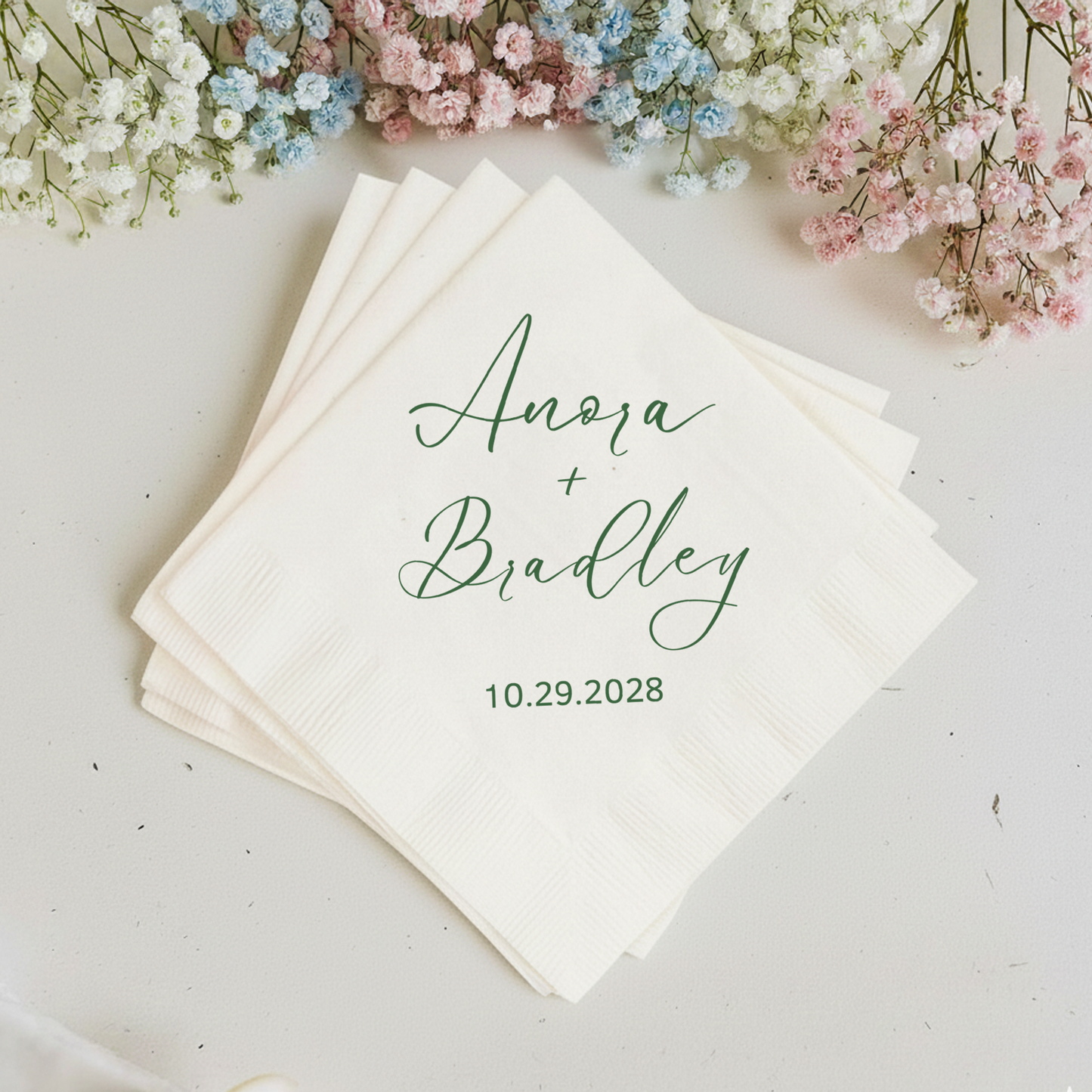 Stack of personalized napkins with names and date, surrounded by small flowers on a light background