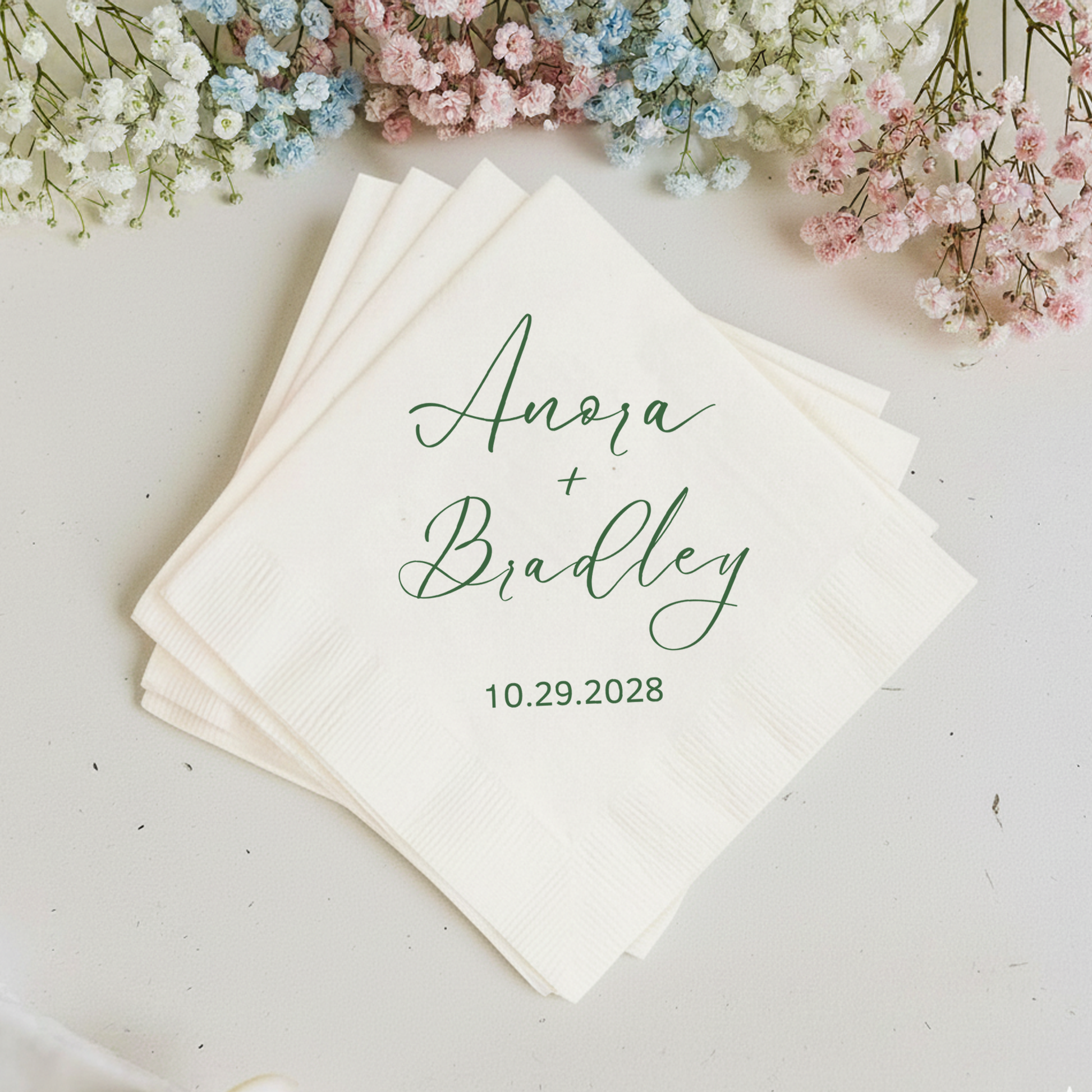 Stack of personalized napkins with names and date, surrounded by small flowers on a light background