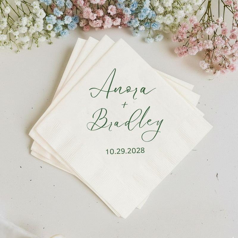 Stack of personalized napkins with names and date, surrounded by small flowers on a light background