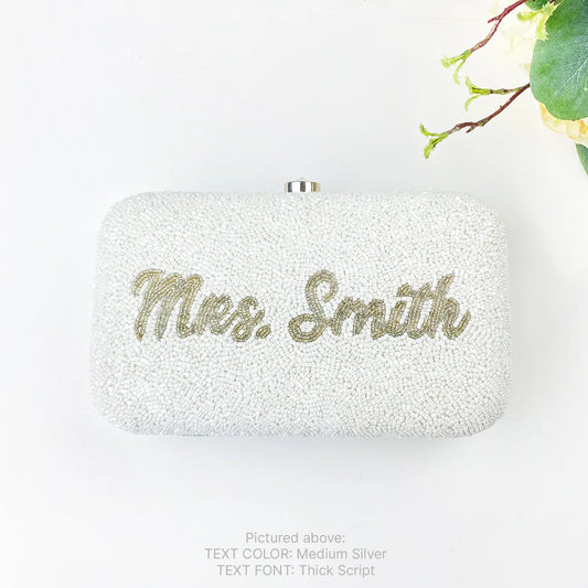 A white clutch bag with the names "Mes. Smith" embossed on it in gold lettering.