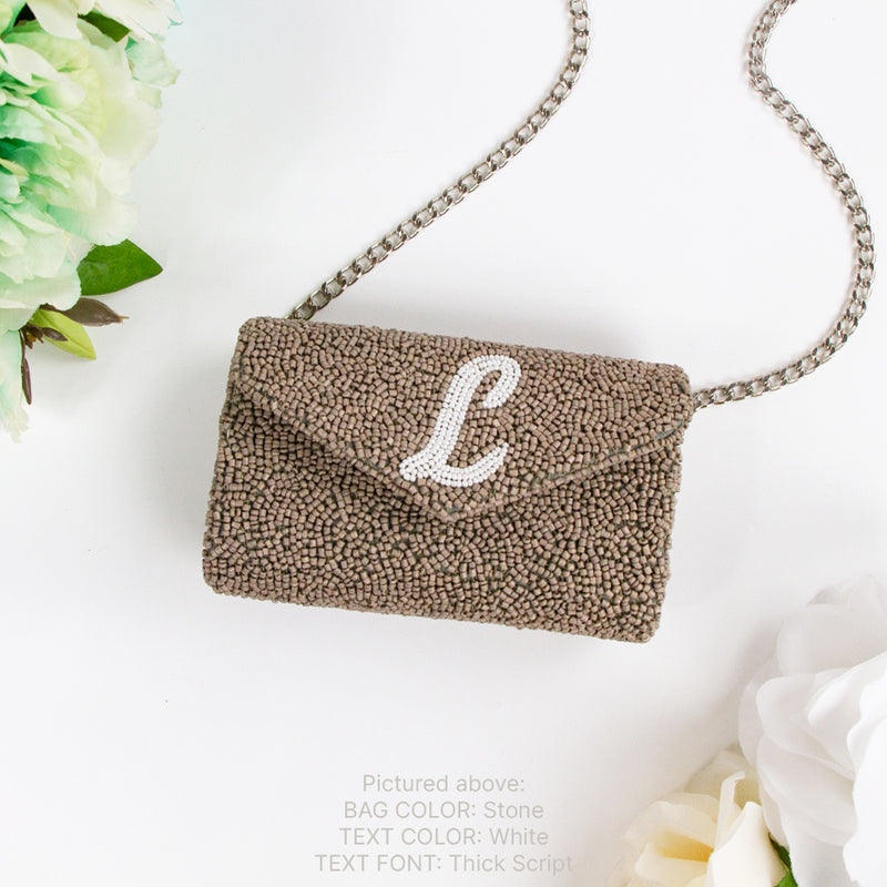 a beaded clutch purse with a monogrammed "L" on it, placed on a white background next to some flowers.