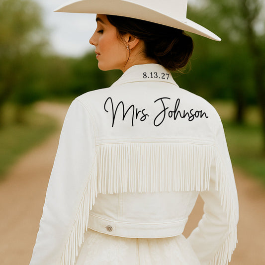 Woman wearing a white fringe jacket with 'Mrs. Johnson' and a date on it, standing outdoors.