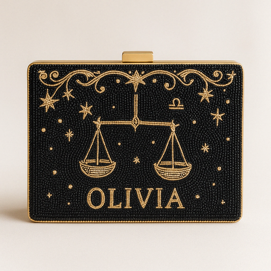 A black clutch bag with gold embellishments, including a design of scales and stars, and the name "OLIVIA" printed on it.