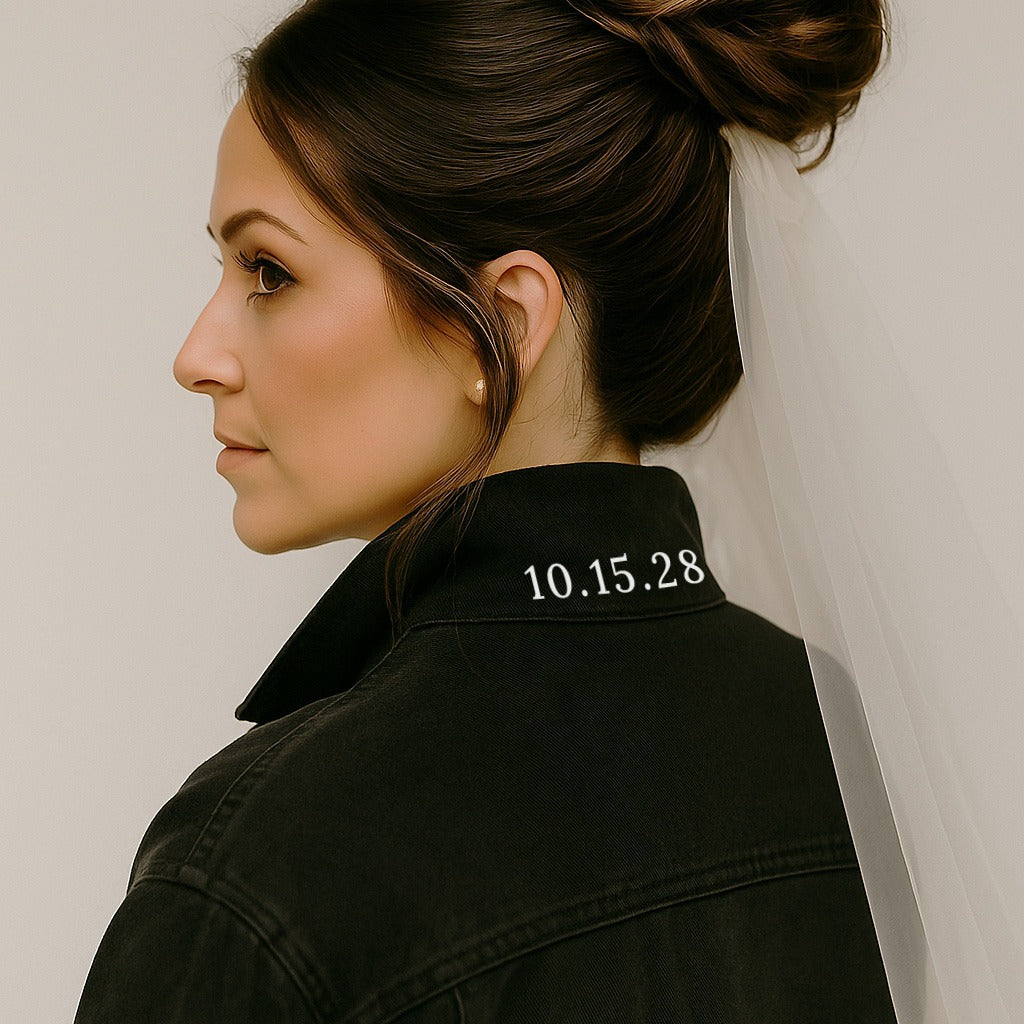 A woman with a bun hairstyle wearing a black jacket with the date "10.15.28" printed on it.