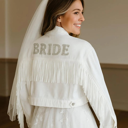 A woman wearing a white fringe denim jacket with the word 'BRIDE' patches on the back, along with a white veil.