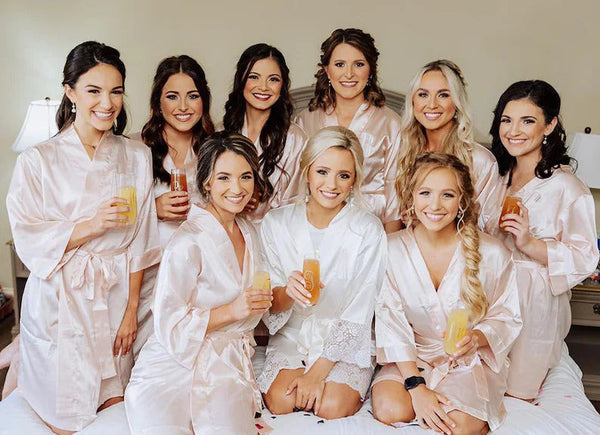 Set of nine matching blush satin bridesmaid robes with the bride in white — getting ready photo