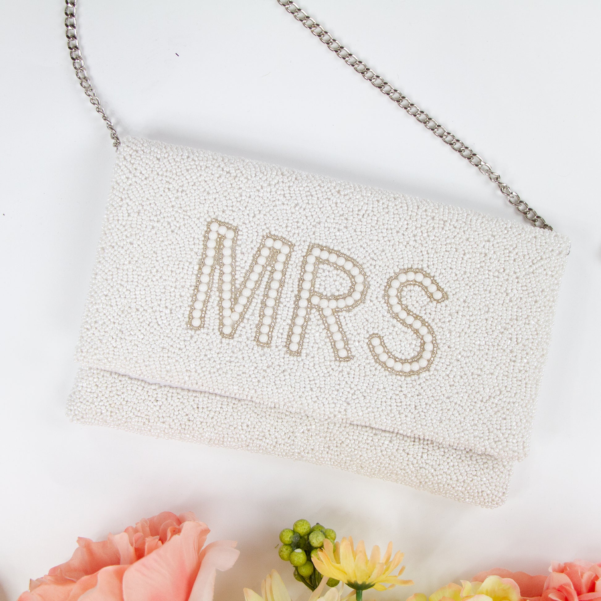 Elegant white MRS Bridal Clutch, handcrafted with intricate beading and a distinctive pattern. Made from durable canvas with a satin finish inside and secured with a magnetic snap closure. Measuring 10 x 6 x 1 inches, this bridal clutch is perfect for holding wedding day essentials and showcases the unique charm and variations of handmade items.
