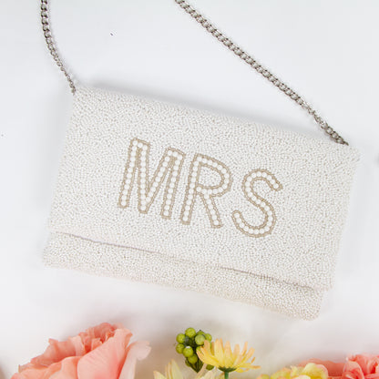 Elegant white MRS Bridal Clutch, handcrafted with intricate beading and a distinctive pattern. Made from durable canvas with a satin finish inside and secured with a magnetic snap closure. Measuring 10 x 6 x 1 inches, this bridal clutch is perfect for holding wedding day essentials and showcases the unique charm and variations of handmade items.